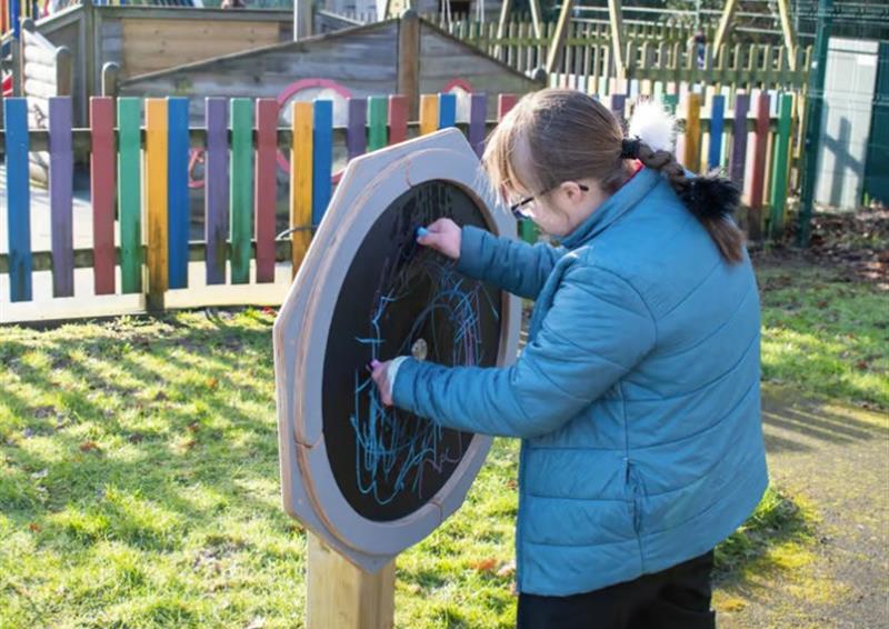 A child playing with a circular chalkboard, outside in a playground